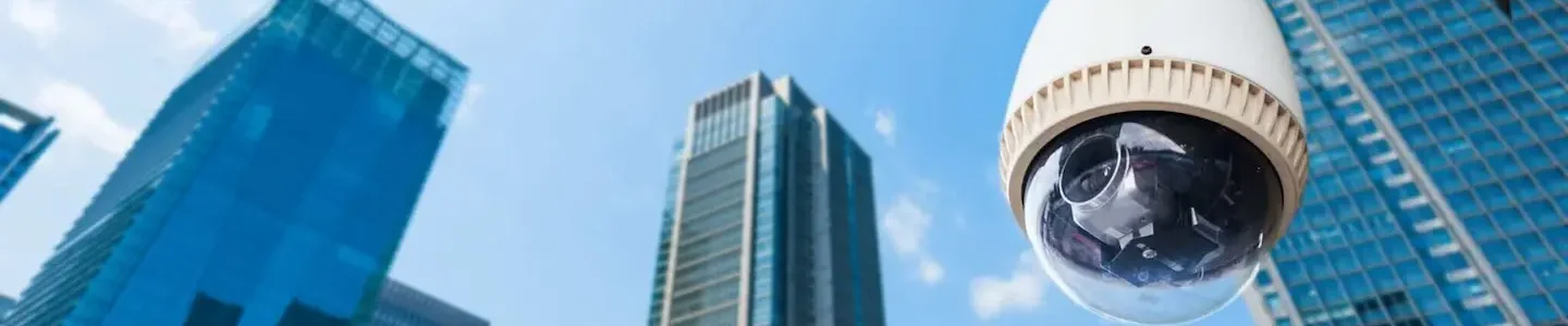 Dome CCTV security camera mounted on a building with city skyscrapers in the background
